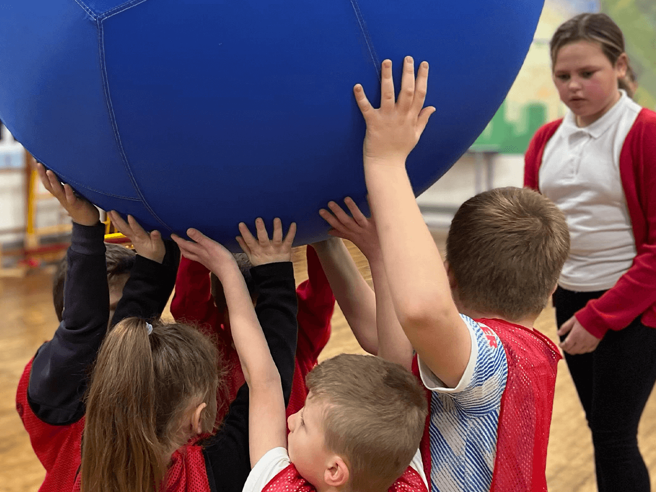 Children in a team-building exercise lifting a large heavy ball.