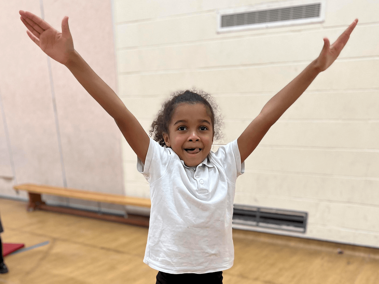 A happy girl finishing off her gymnastics move with her arms raised.