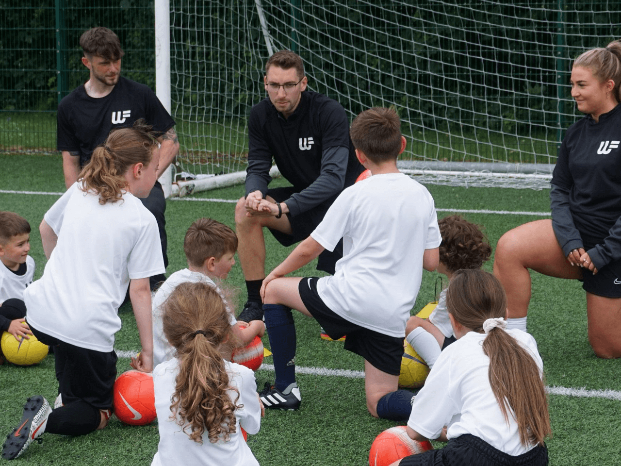 A group of children kneeling as they listen to their football coaches.