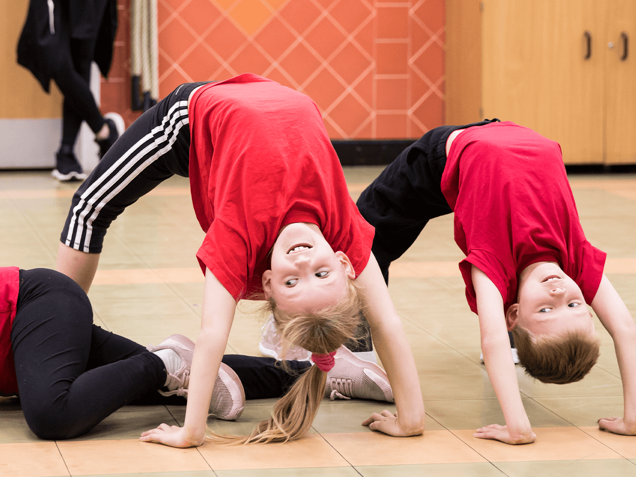 Two children performing a reverse bridge while a girl crawls underneath them.