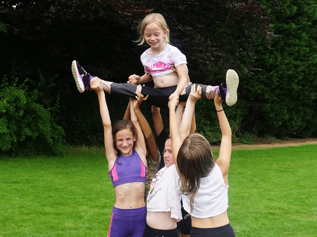 Young female cheerleaders lifting one girl above their heads together as she does the splits.