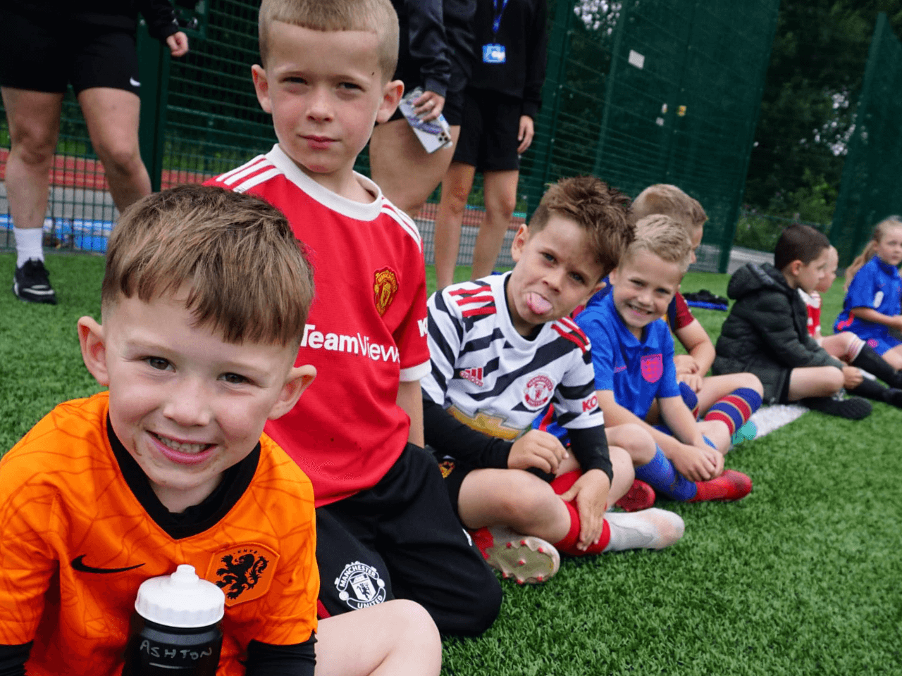 A group of happy boys sat on a football field awaiting their coach's instructions.