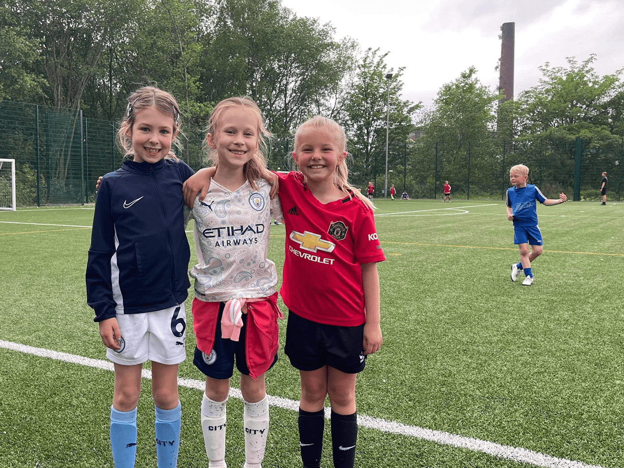 Three girls with arms around each other posing for a photo on the football field.