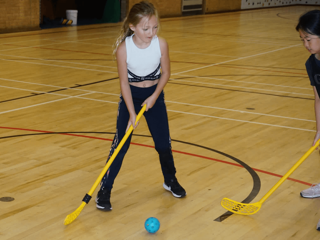 A girl playing hockey in the sports hall.