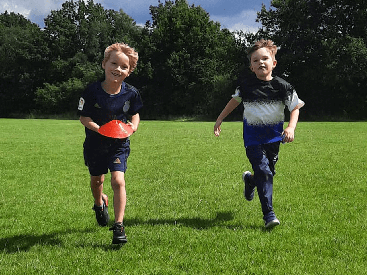 Two boys collecting cones on a sports field.