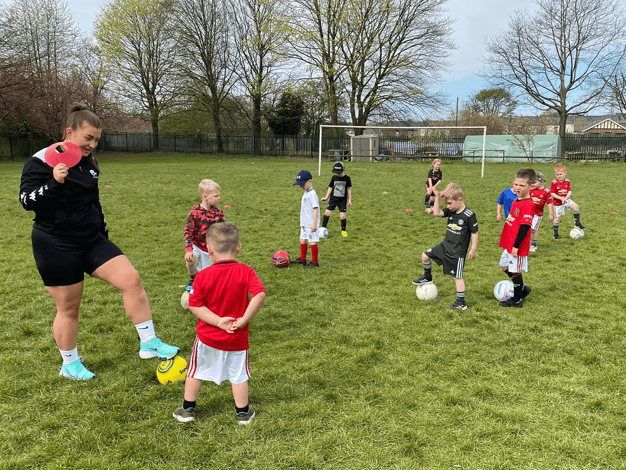 A coach teaching a group of young children how to dribble a football.