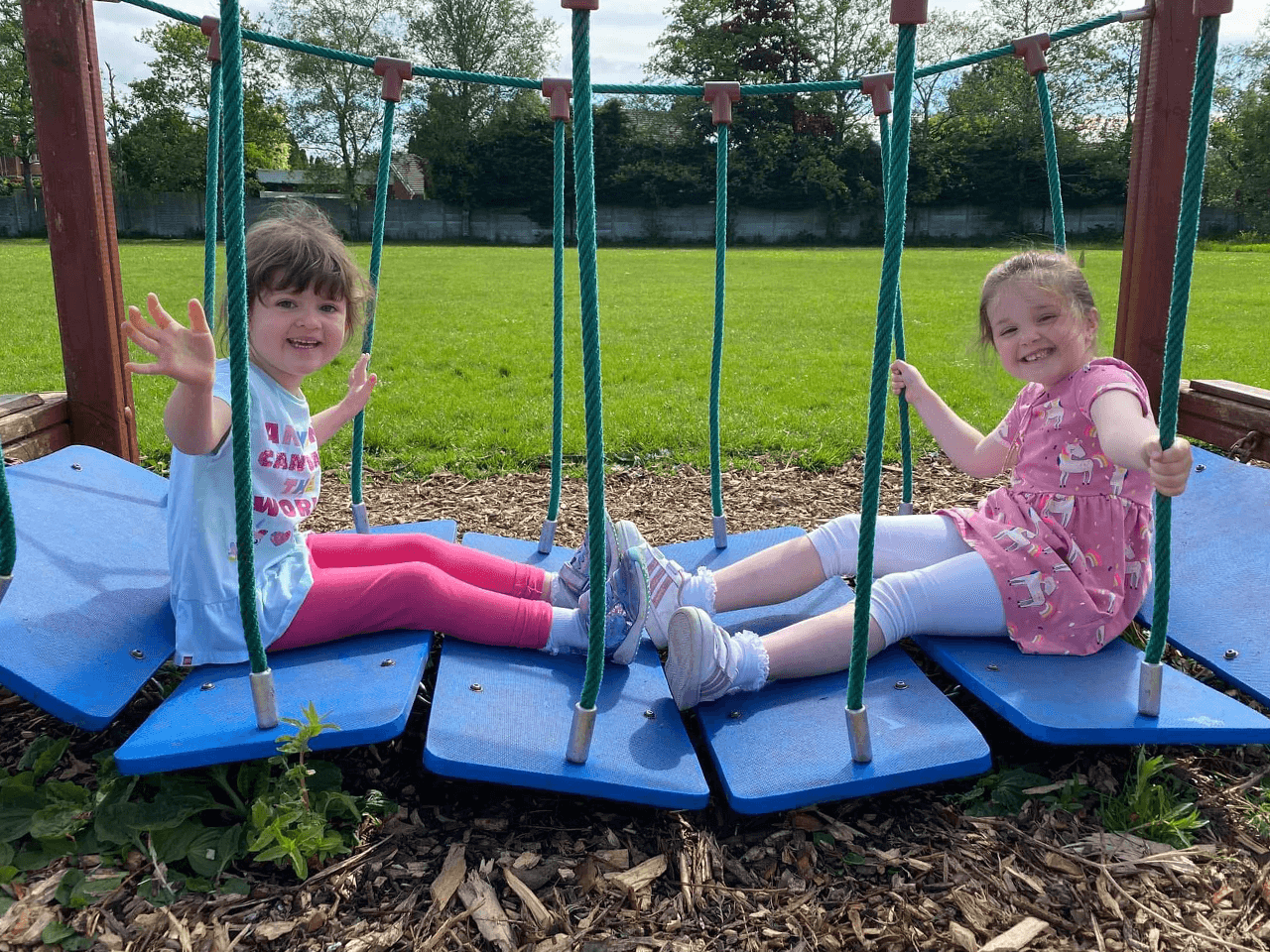 Two girls sat on a play area bridge walkway.
