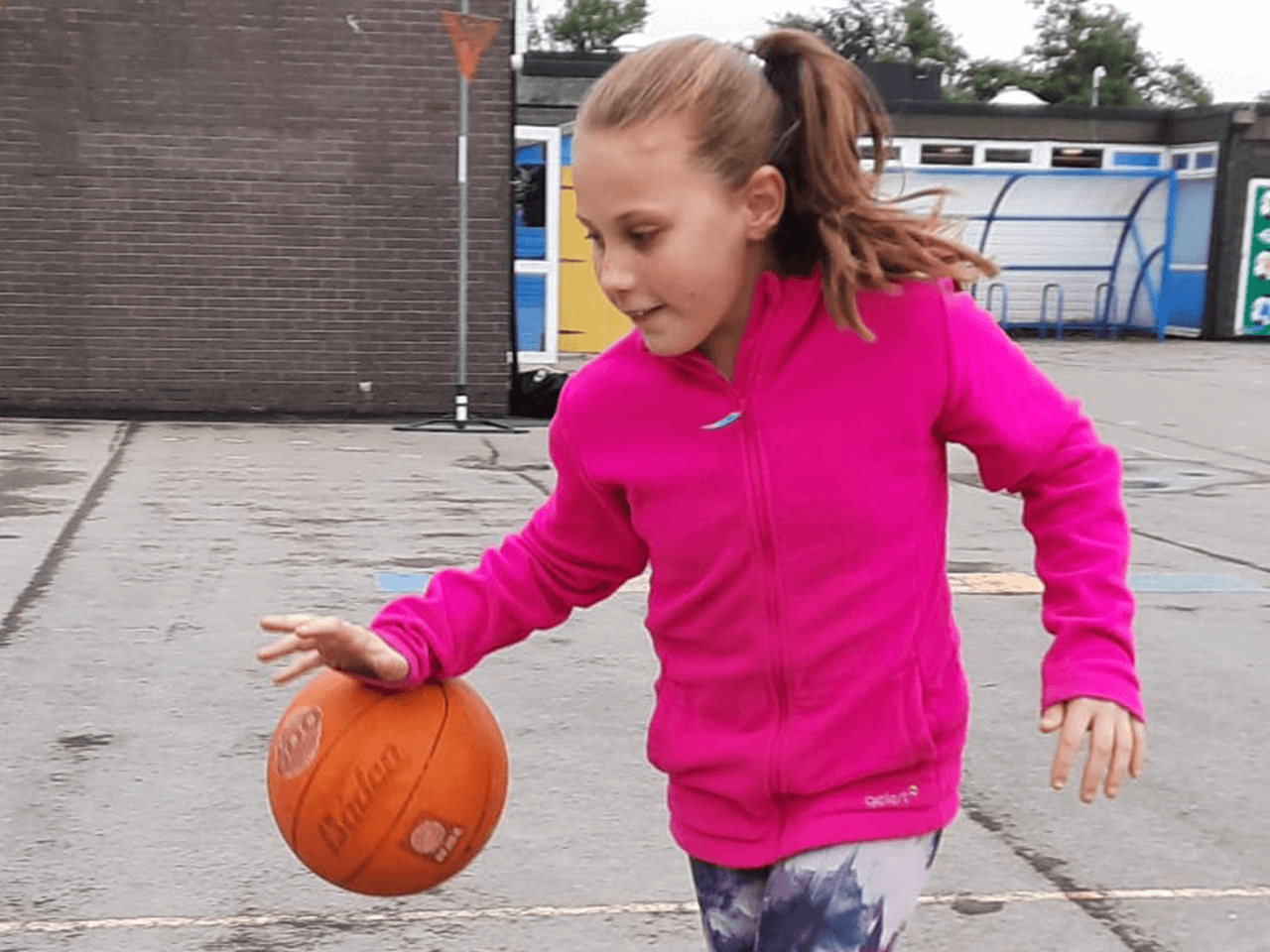 A girl dribbling a basketball in a playground.