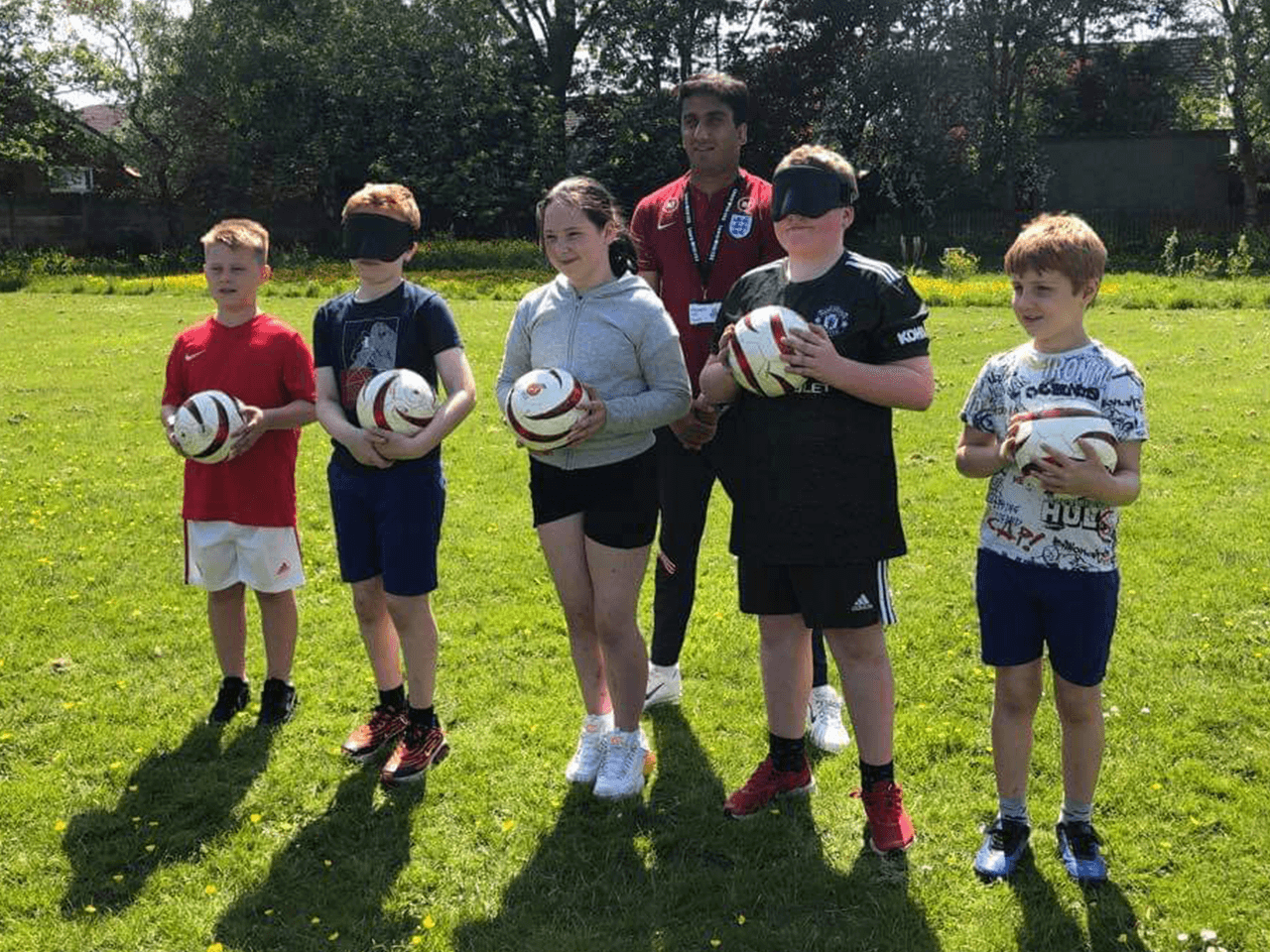 A group of children wearing blindfolds experiencing blind football.