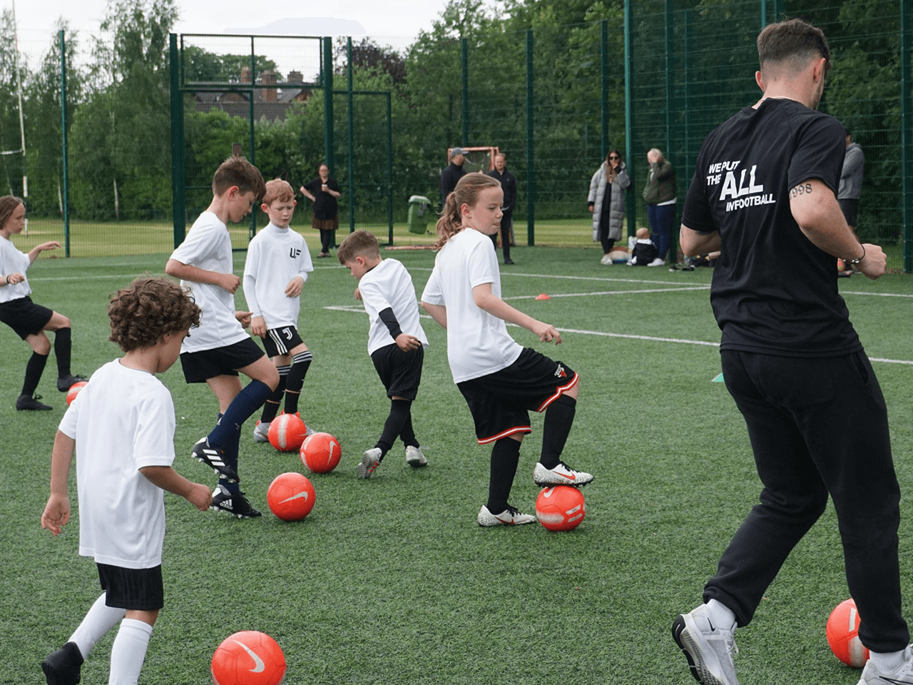 Children dribbling in football drills with their coach.