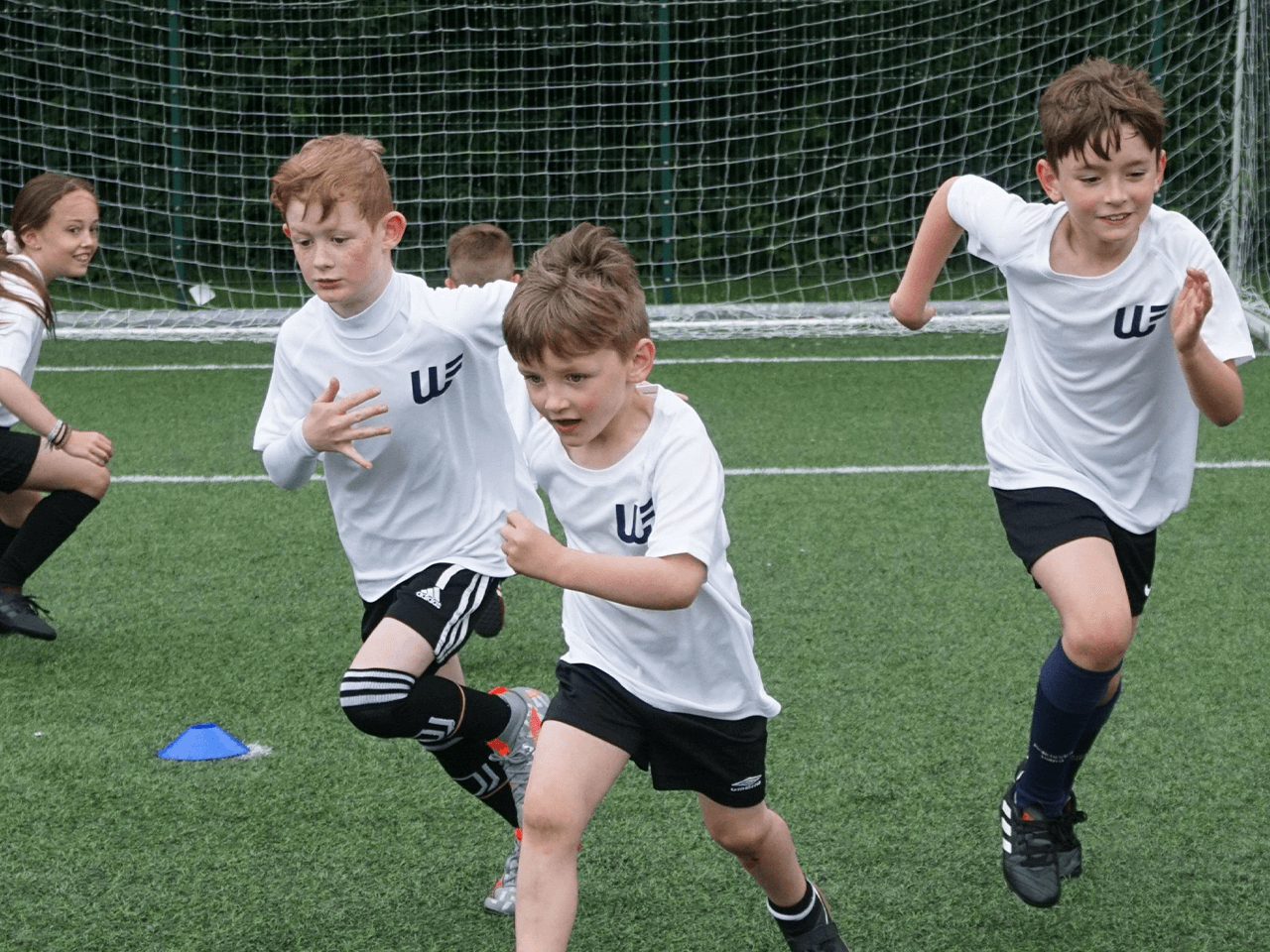 A group of children running in football drills.