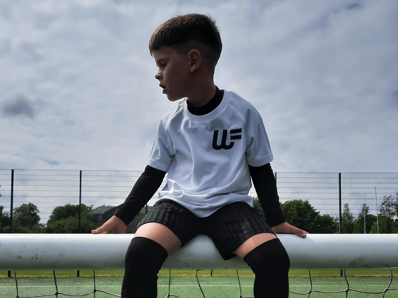 A boy sat on the crossbar of some football posts.