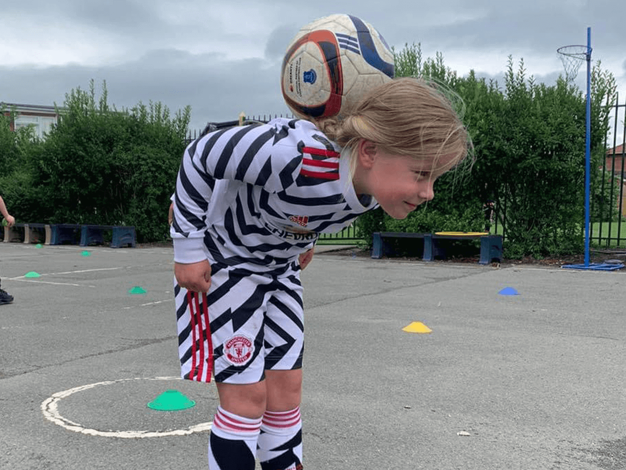 A young girl balancing a football on the back of her neck.