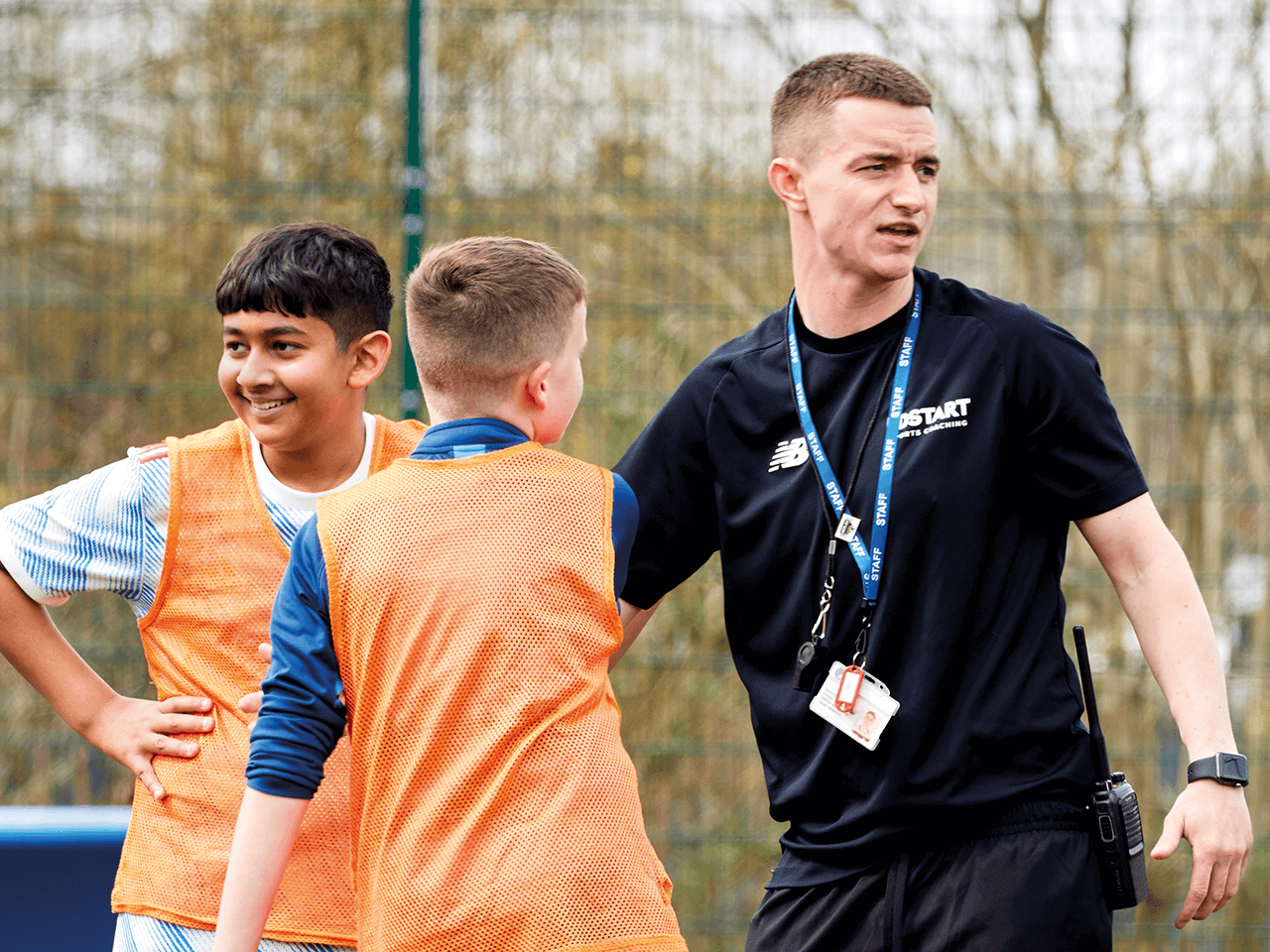 A sports coach on the pitch with two boys in training vests.