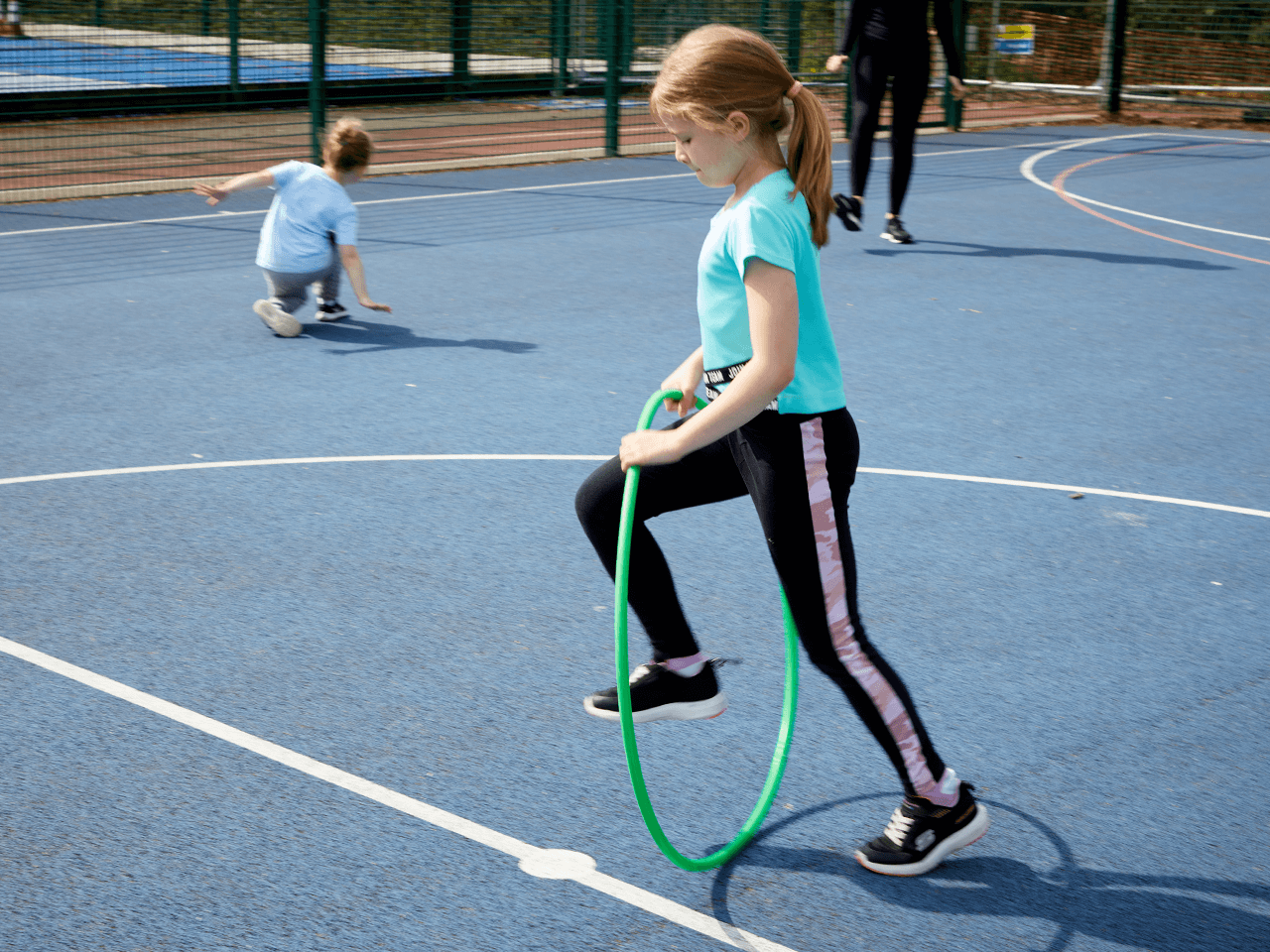 A girl skipping through a hula hoop in a playground.