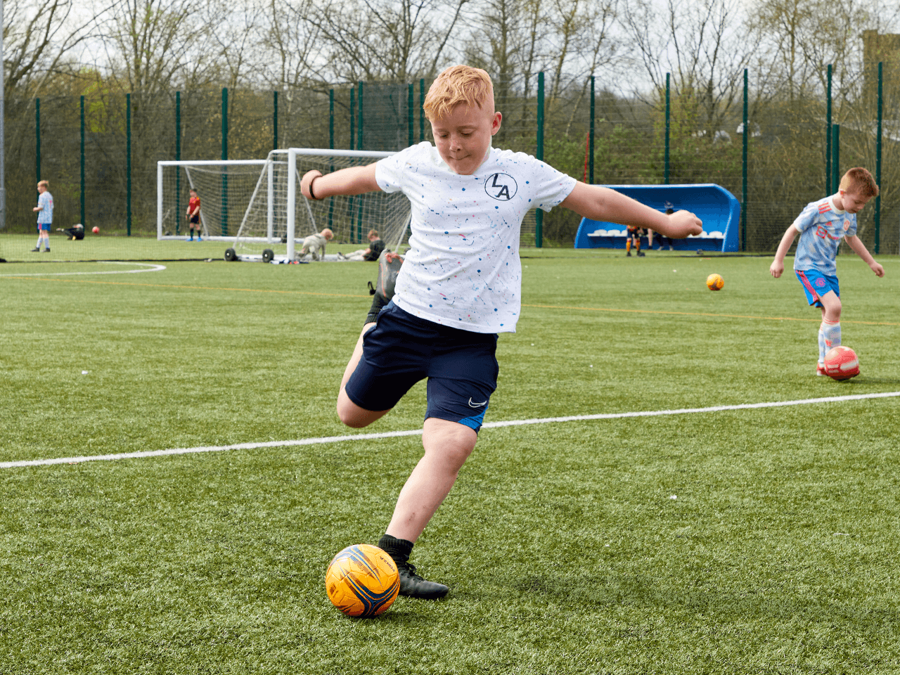 A boy about to kick a football on a pitch.