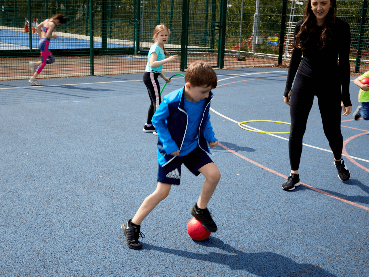 A boy showing off his football skills in front of a coach on the playground.