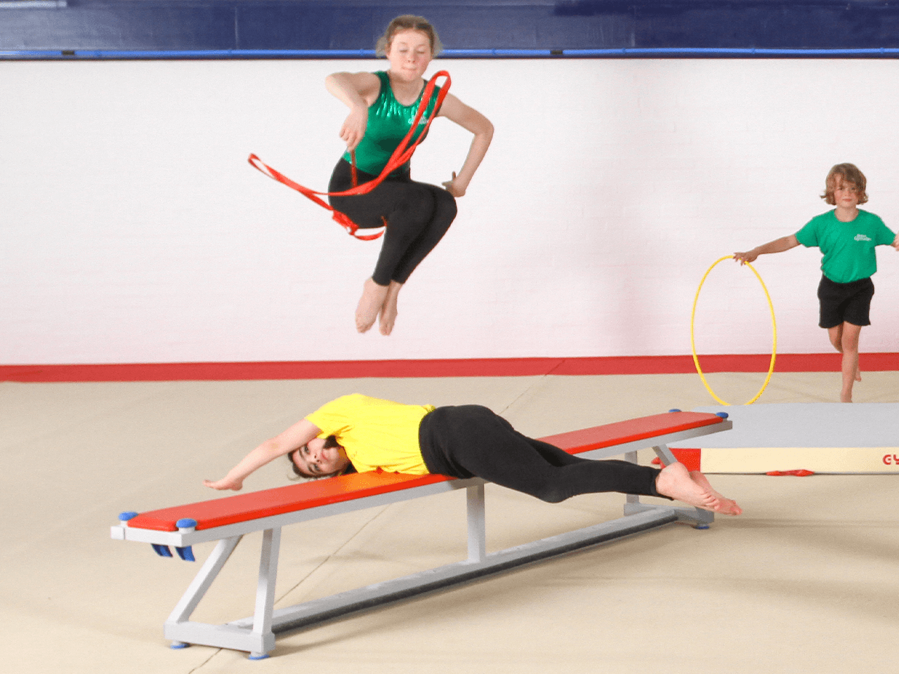 A group of children performing gymnastics moves - one lying balancing on a bench.