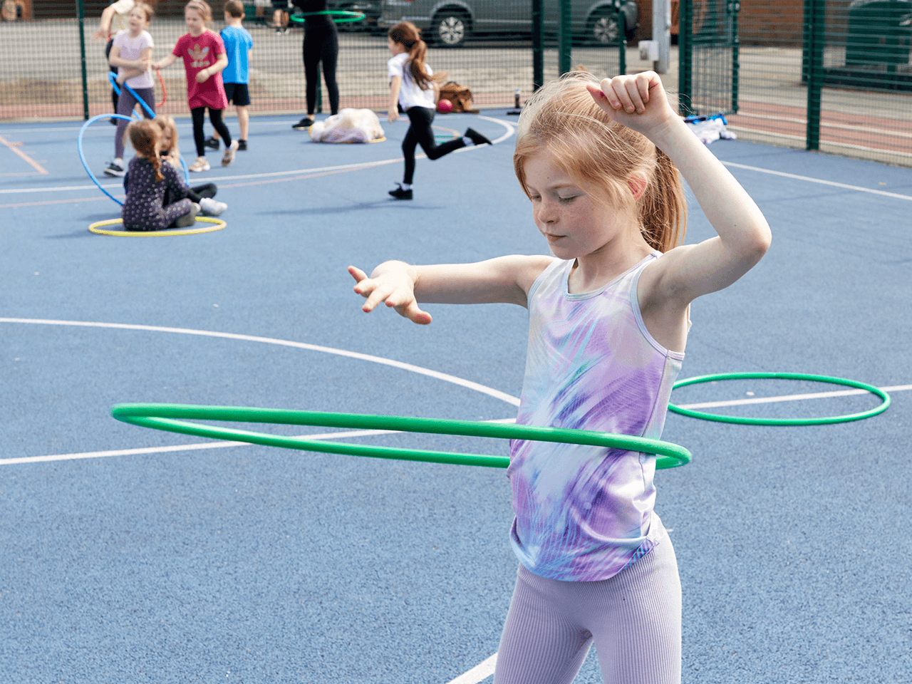 A girl focusing whilst hula hooping in a playground.