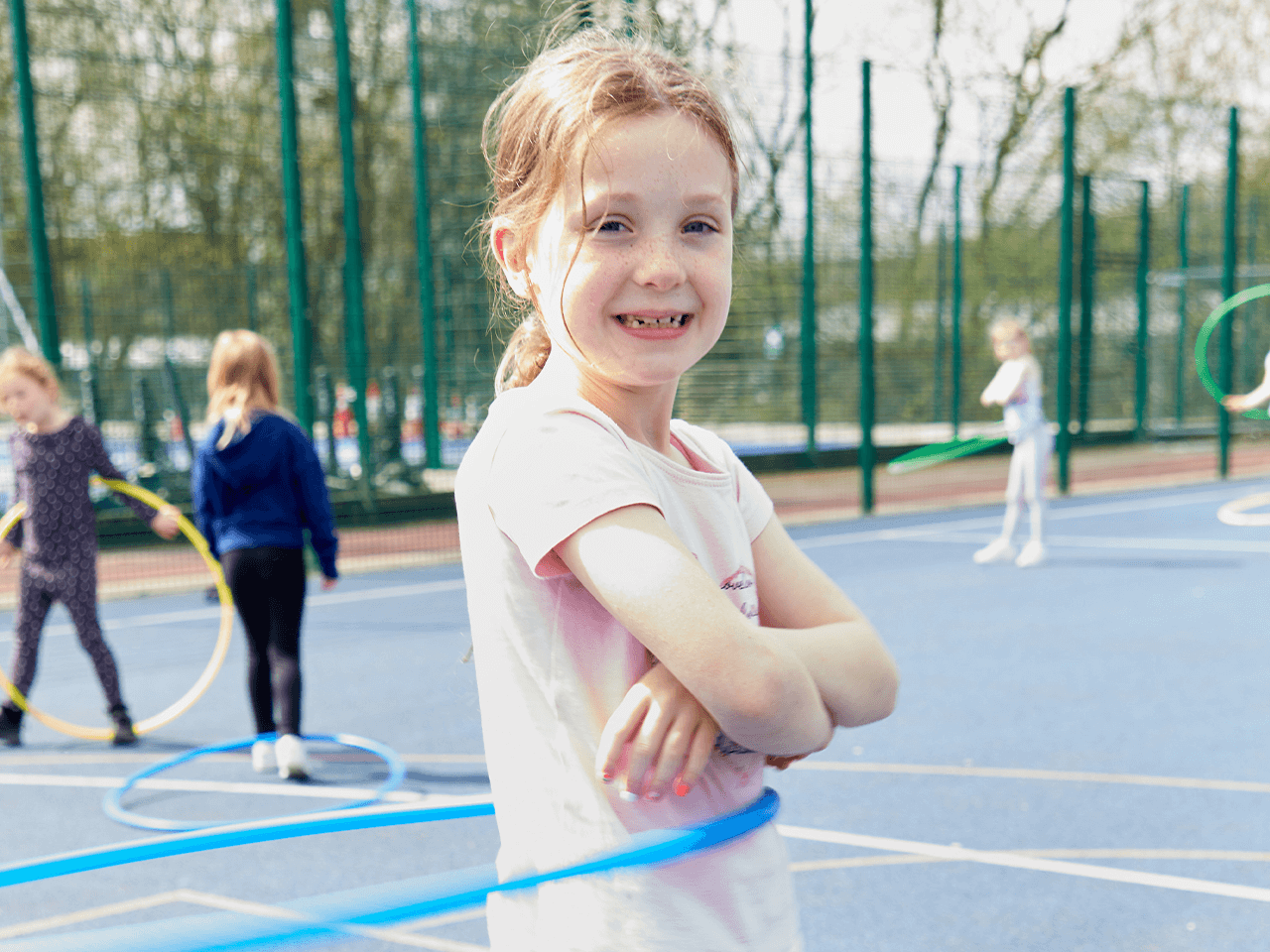 A smiling girl posing as she's hula hooping.