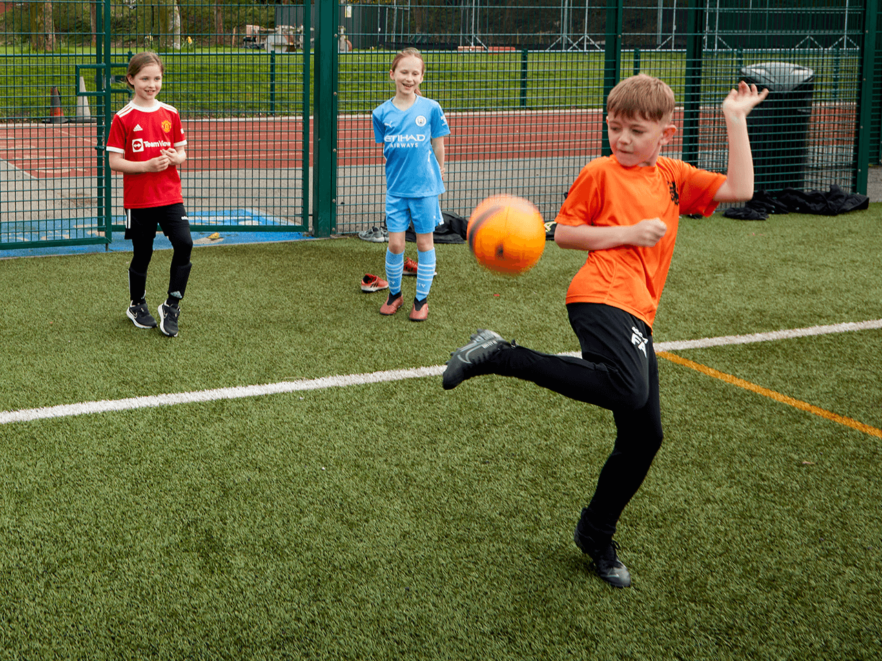 Boy trying a fancy football flick as two girls watch.