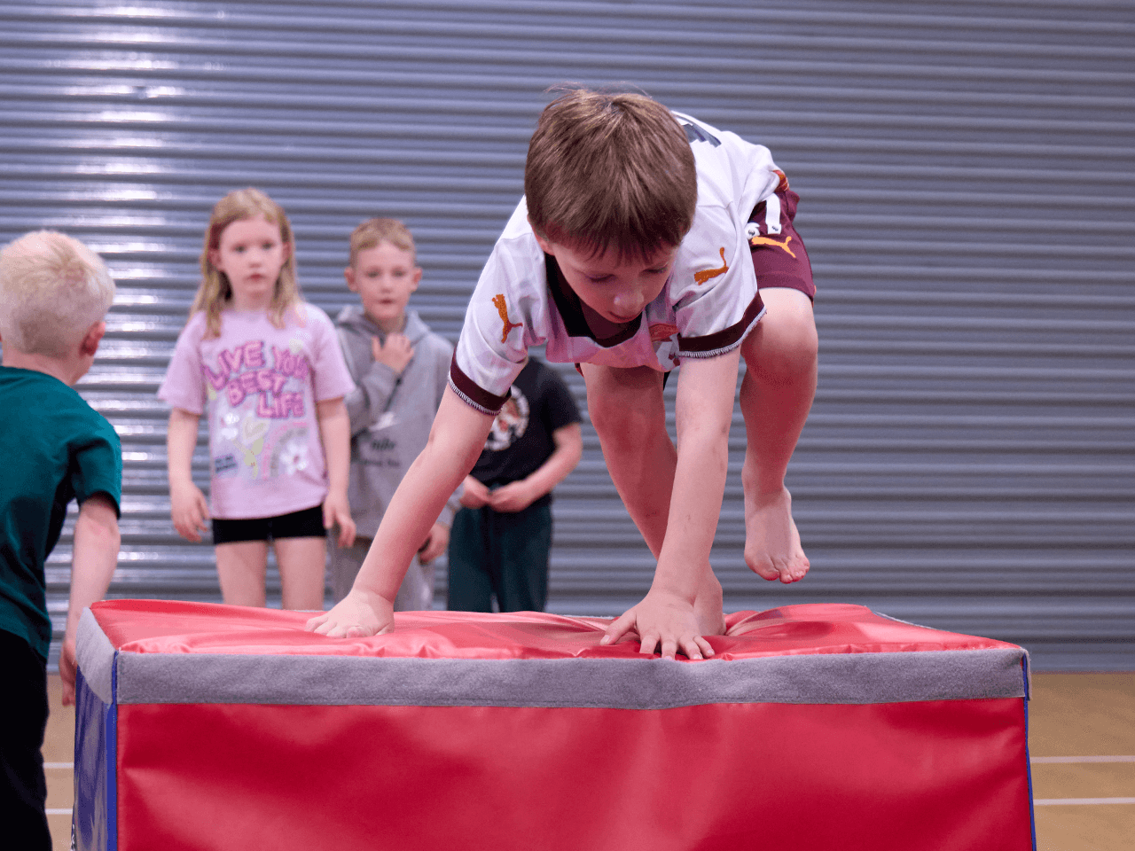 A boy climbing over a gymnastics box.