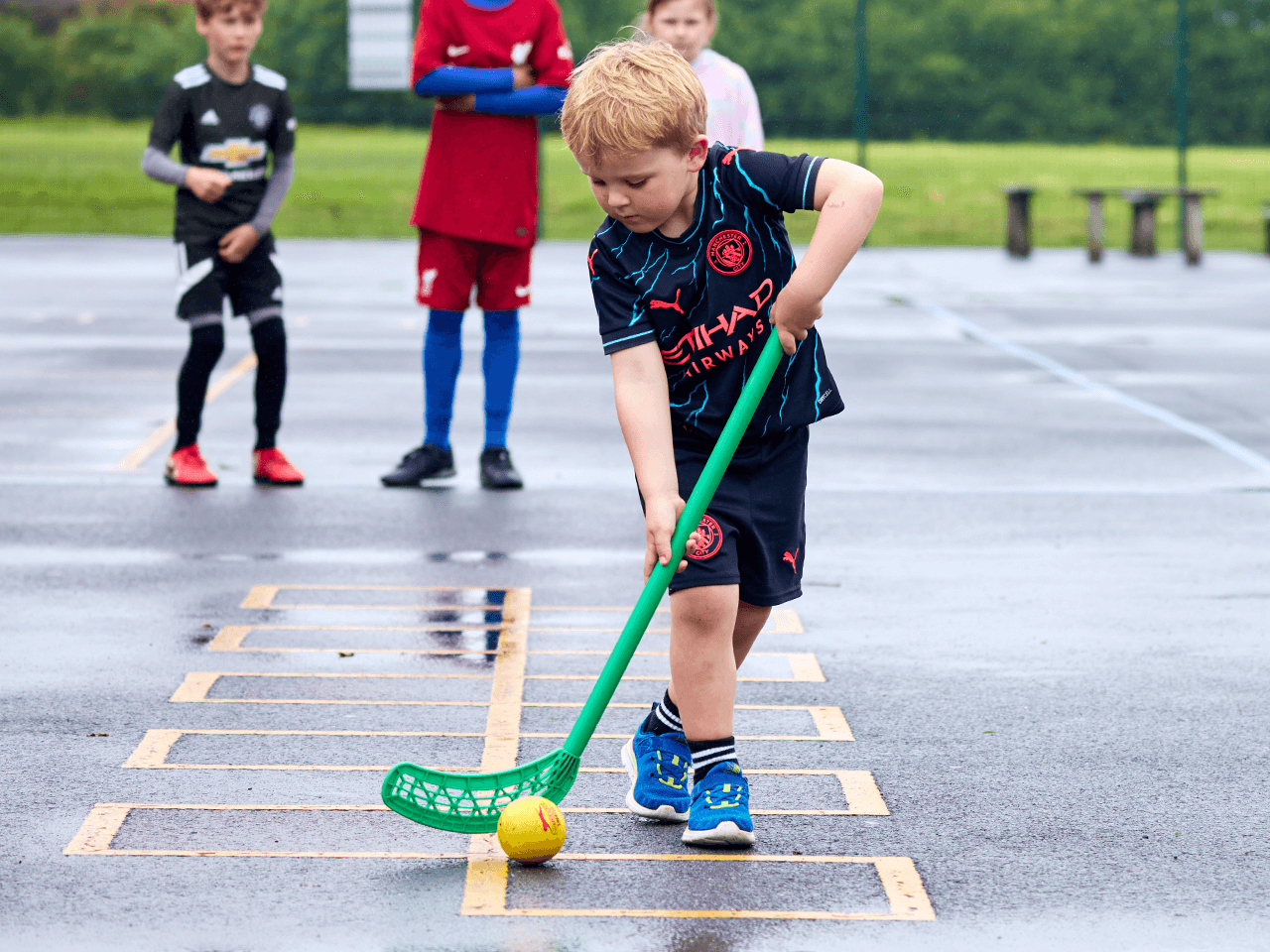 A boy dribbling a ball with a hockey stick.