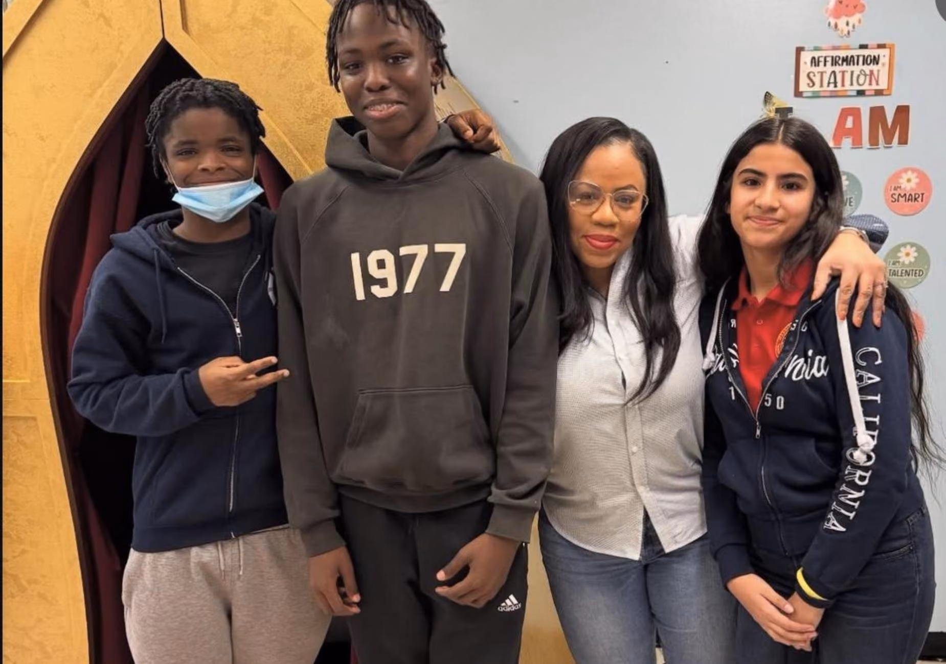 Teacher posing with three students near affirmation station display