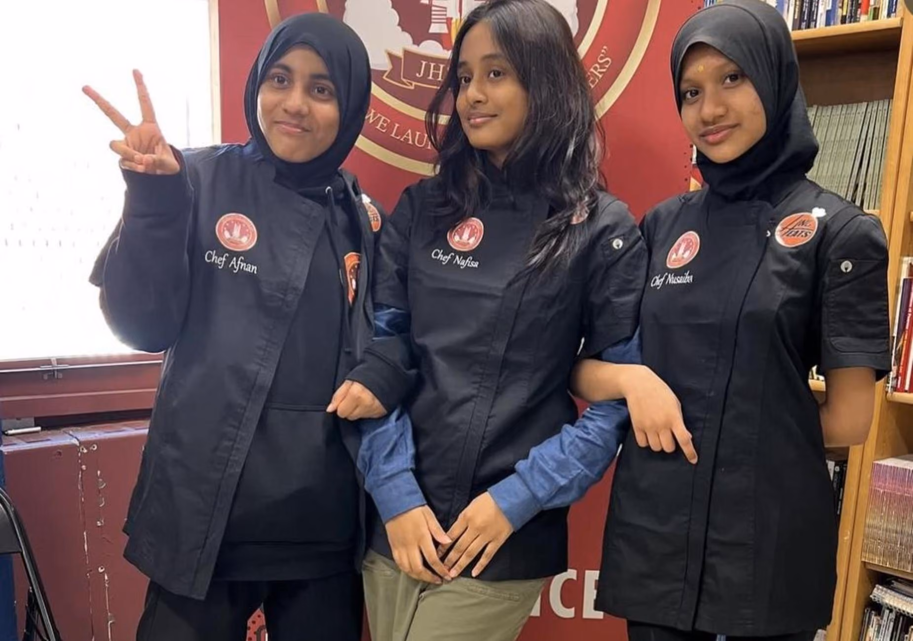 Three student chefs in black chef jackets posing together at school