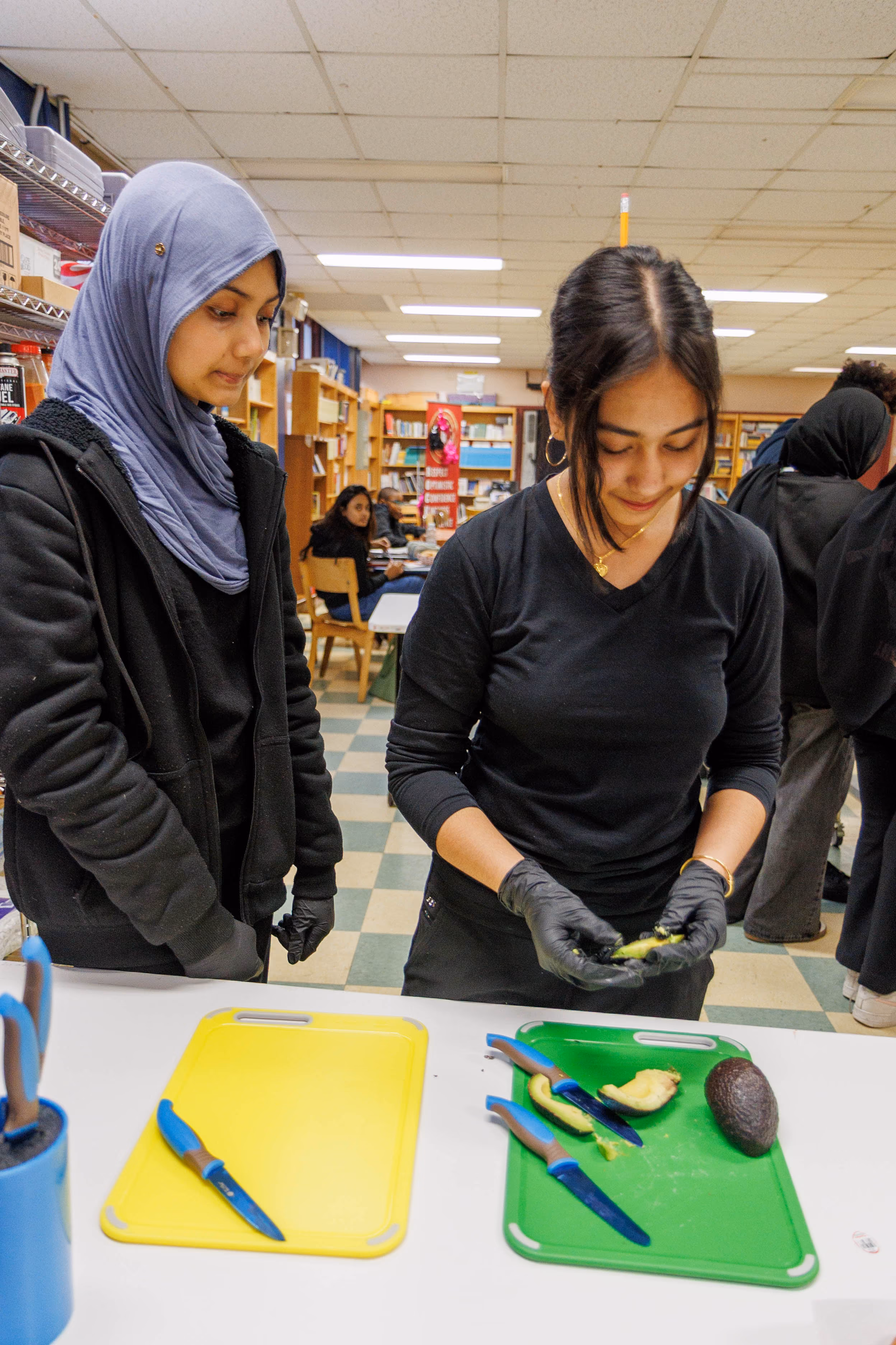 Two students cutting avocado on cutting boards in classroom