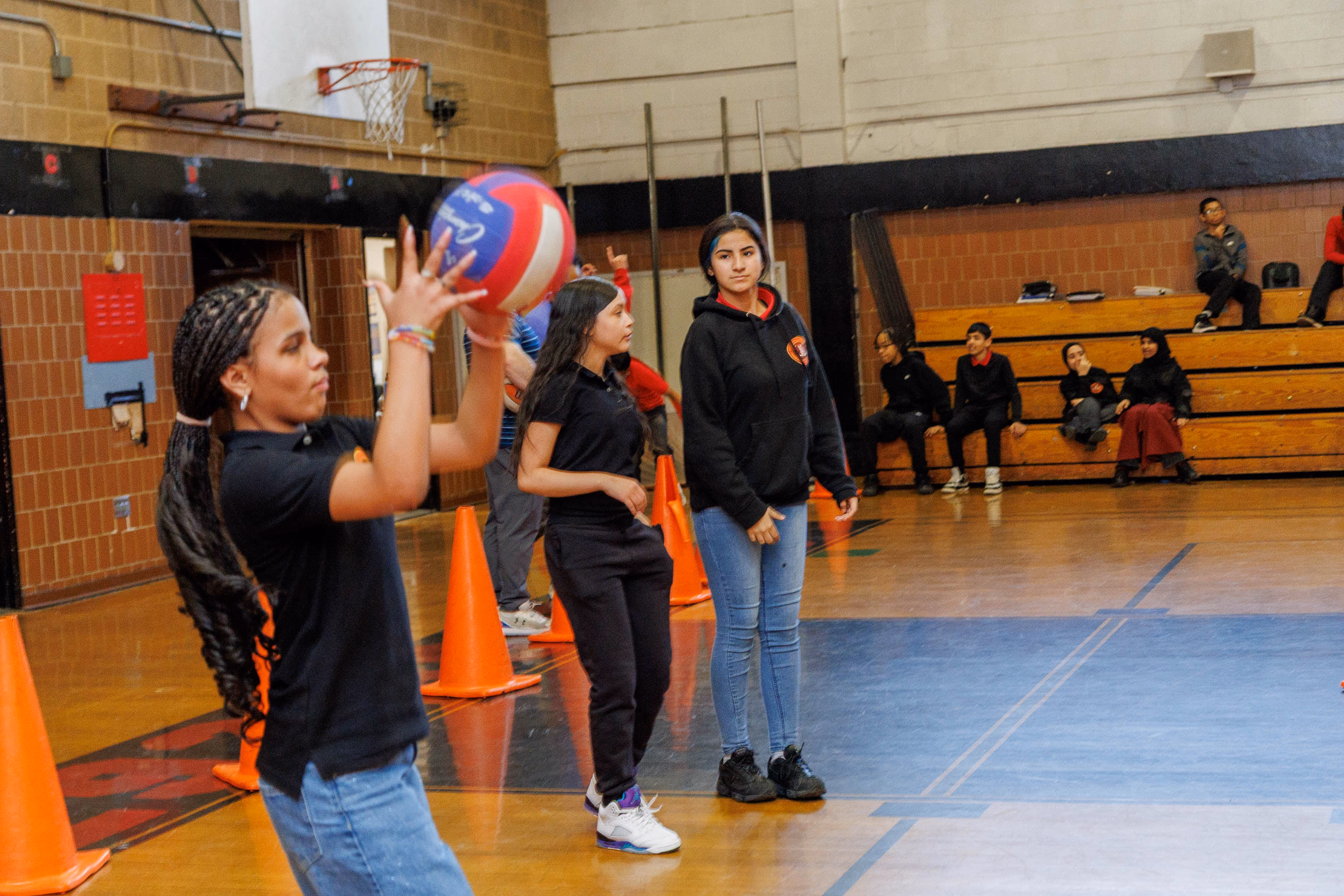 Students practicing volleyball drills in school gymnasium with cones