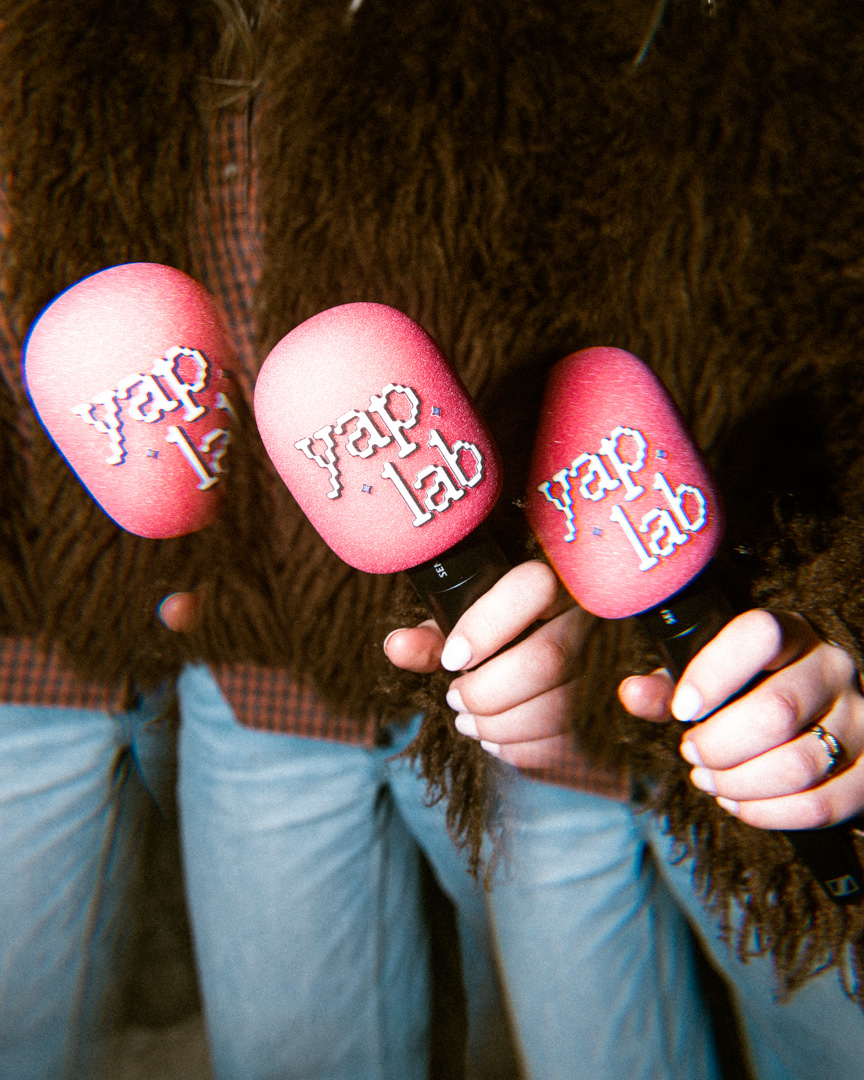 Drie microfoons met rode hoezen en de tekst 'yap lab' worden vastgehouden door personen met bruine jassen en blauwe jeans.