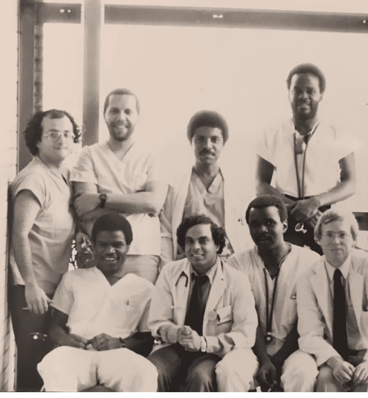 Black-and-white photo of seven medical professionals posing together, some wearing white coats and stethoscopes.