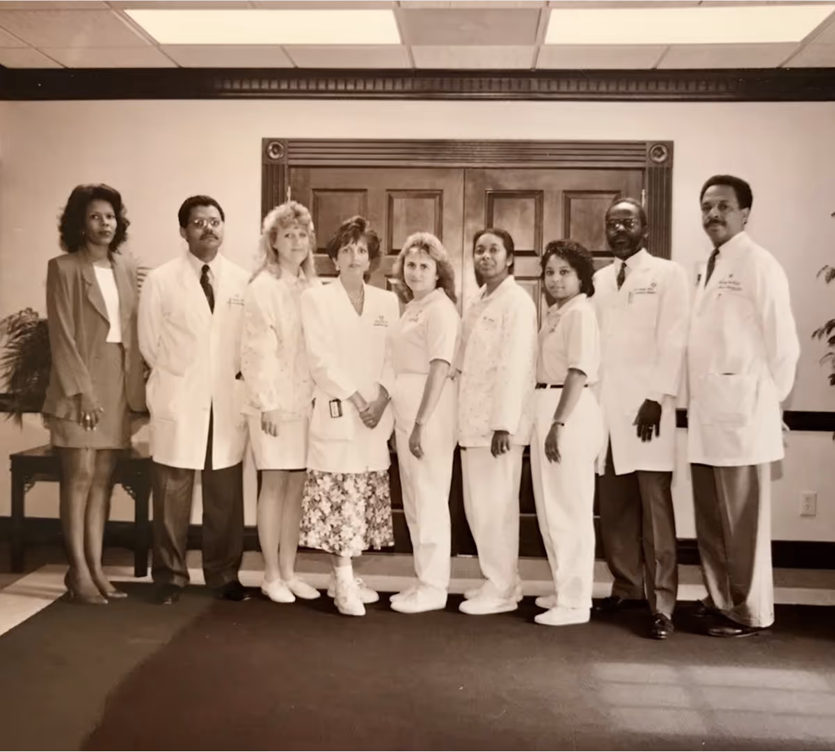 Black-and-white photo of seven medical professionals posing together, some wearing white coats and stethoscopes.