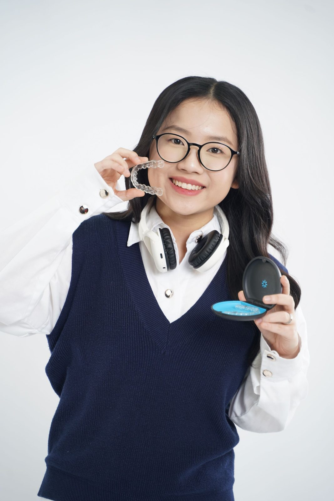 A patient smiling and holding a clear aligner and its case