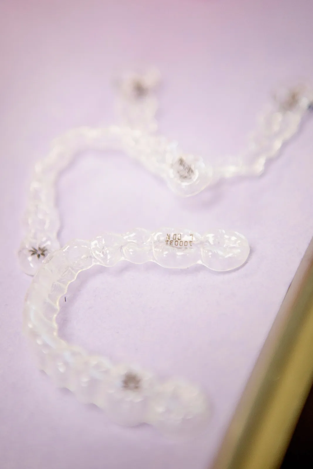 Close-up of two clear dental aligners on a light purple surface.