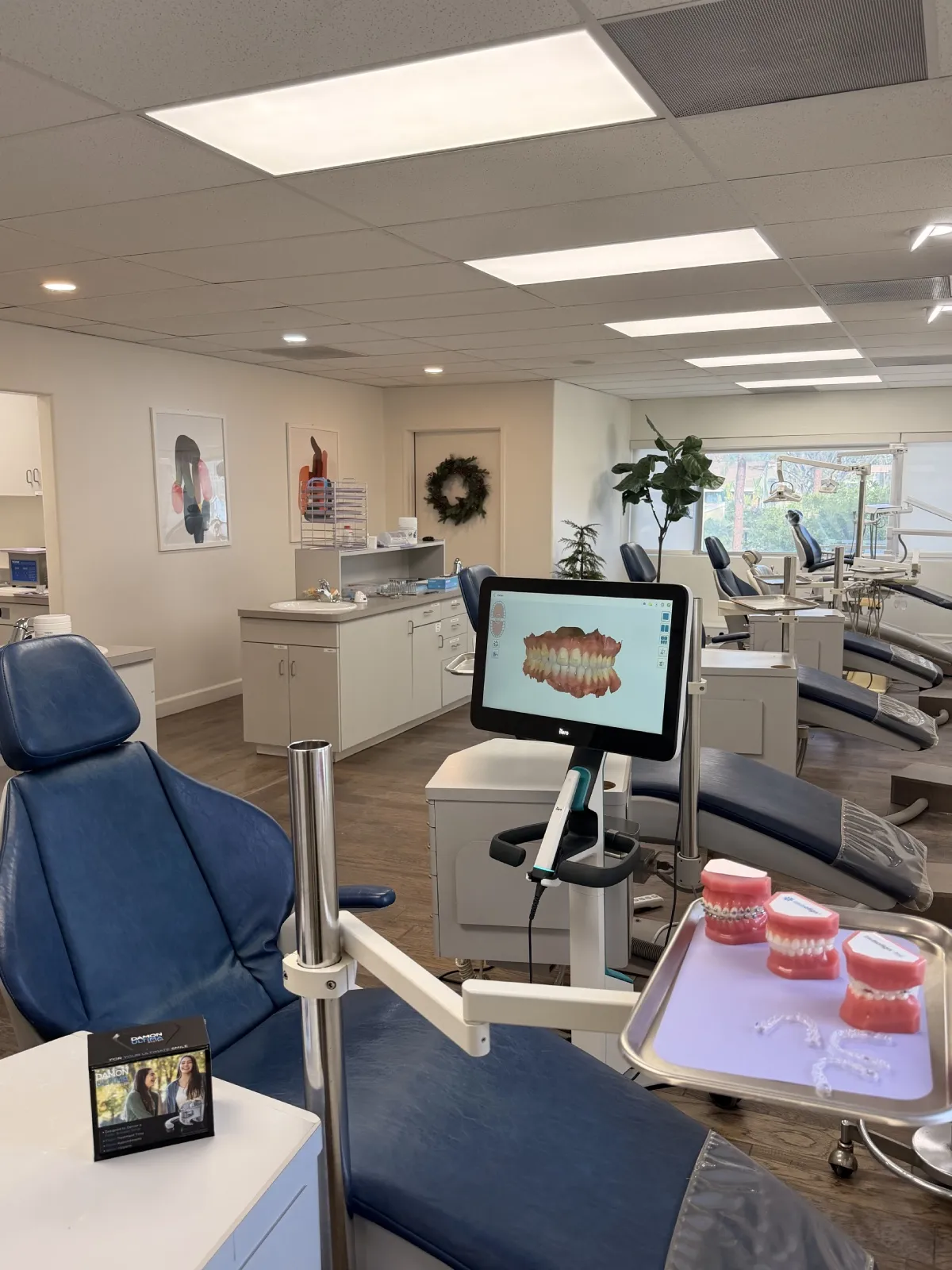Dental clinic with blue dental chairs, a monitor displaying a 3D dental model, and trays with dental molds and clear aligners.