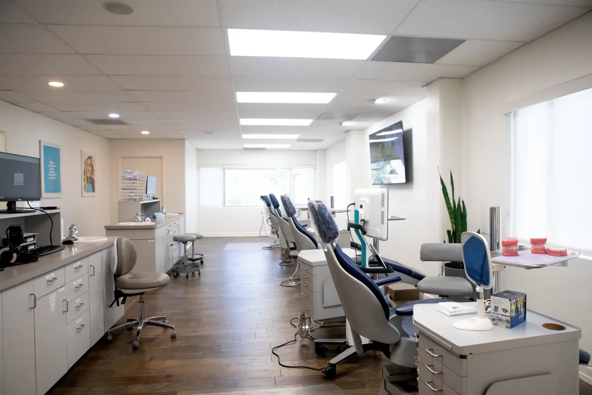Modern dental office with several dental chairs, workstations, and bright overhead lighting.
