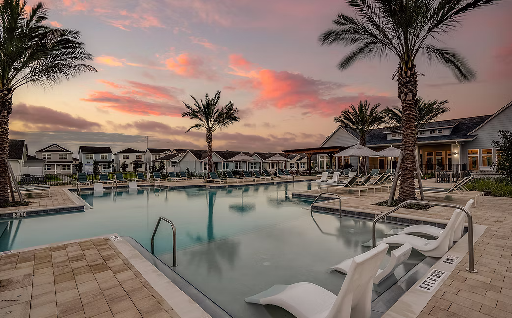 Outdoor swimming pool with lounge chairs and palm trees at sunset in a residential community.