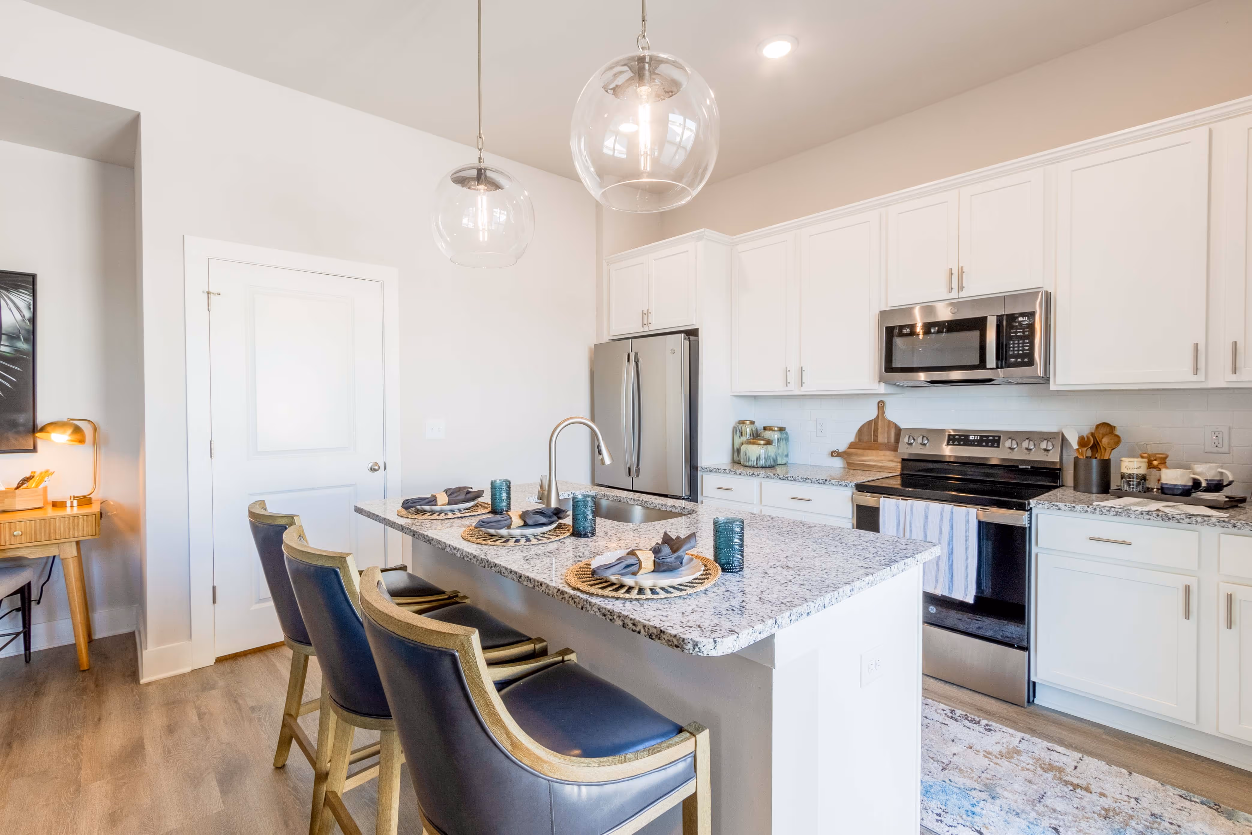 Modern kitchen with white cabinets, granite island, three stools, stainless steel appliances, and pendant lights.
