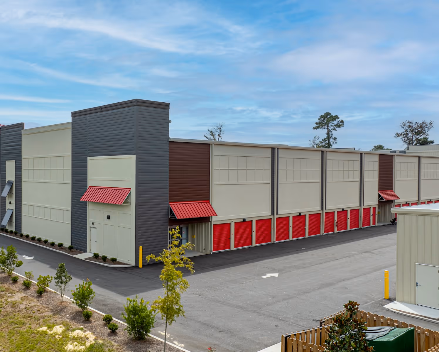 Modern self-storage facility with beige walls and red roll-up doors under a blue sky.