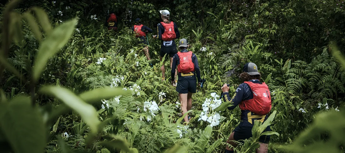 Runners in red packs climbing through dense jungle in Colombia