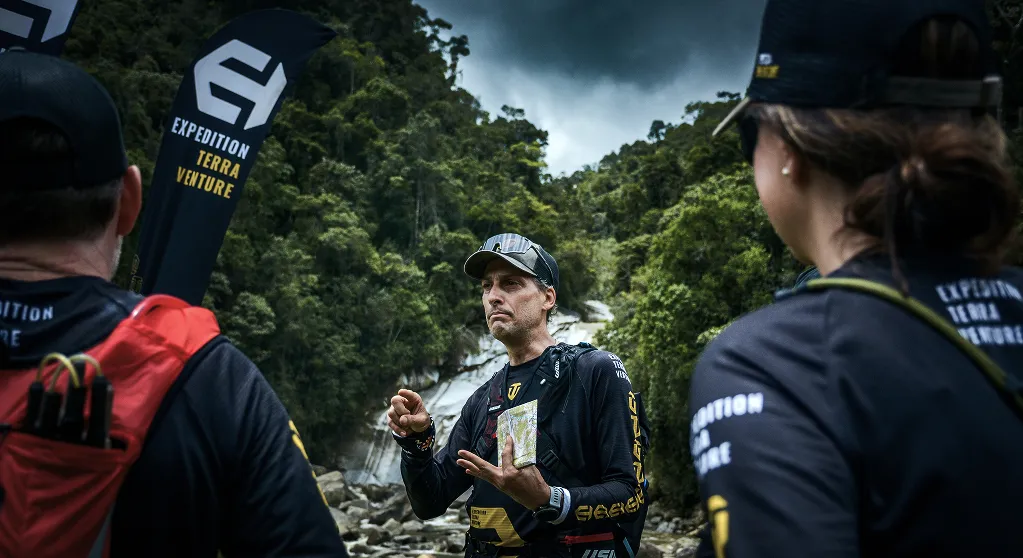 Expedition guide briefing runners with a map in front of a waterfall