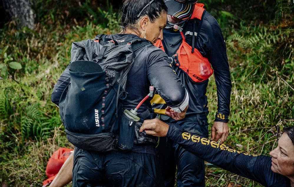 Teammates adjusting a USWE hydration pack on the trail