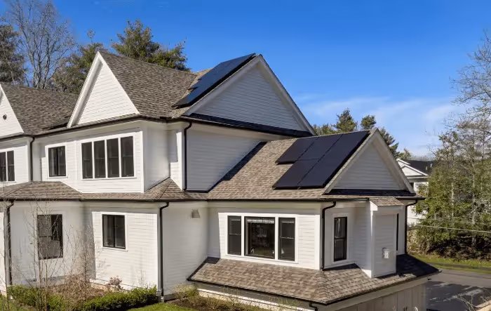 Modern white two-story home with black solar panels installed on the roof under a clear blue sky.
