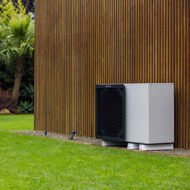 A daikin altherma heat pump outside a brown wooden wall next to the grass