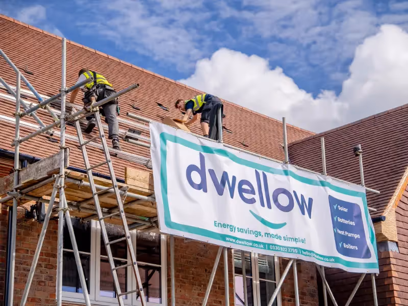 Dwellow solar panels installers on the roof of a house with a dwellow banner hanging from scaffolding.