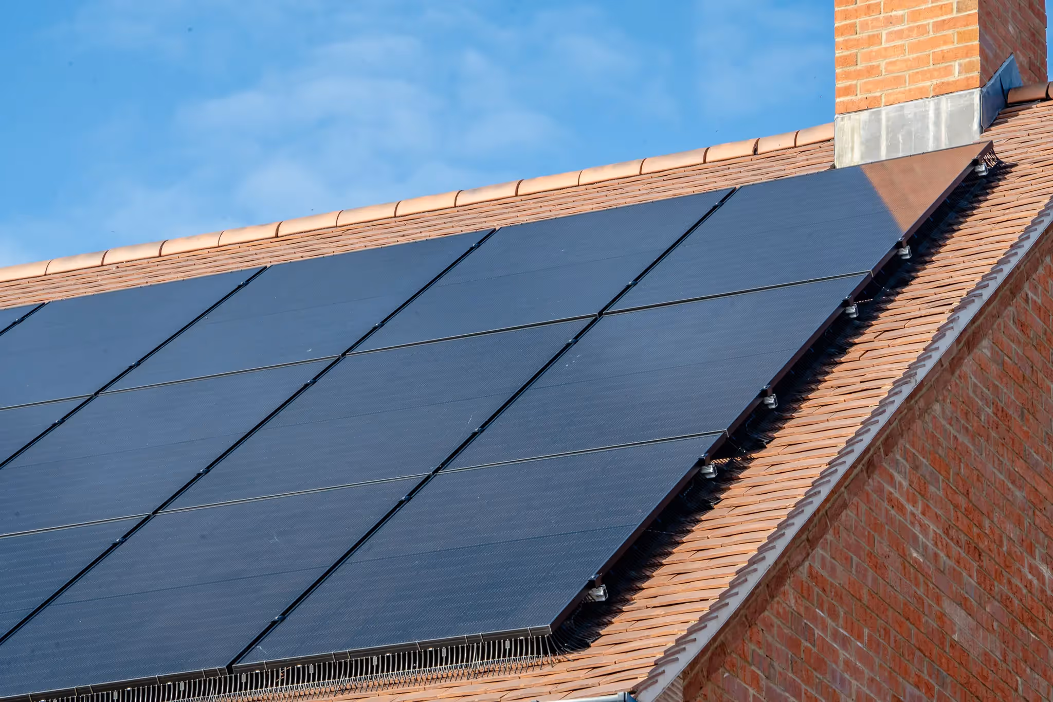 Image of black solar panels on a residential roof with blue sky in the background