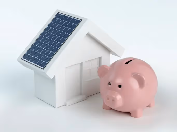 A picture of a piggy bank next to a model house with a solar panel on the roof