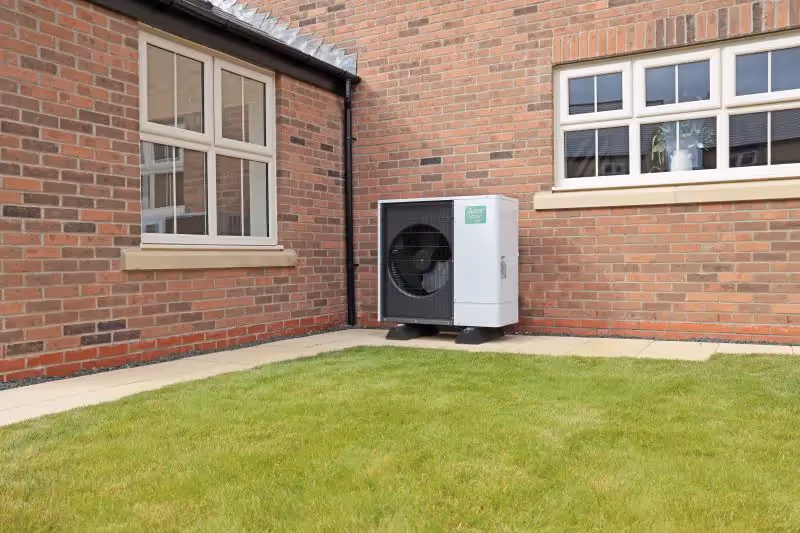 image of the mitsubishi ecodan heat pump in a garden, by the wall of the house, under a window